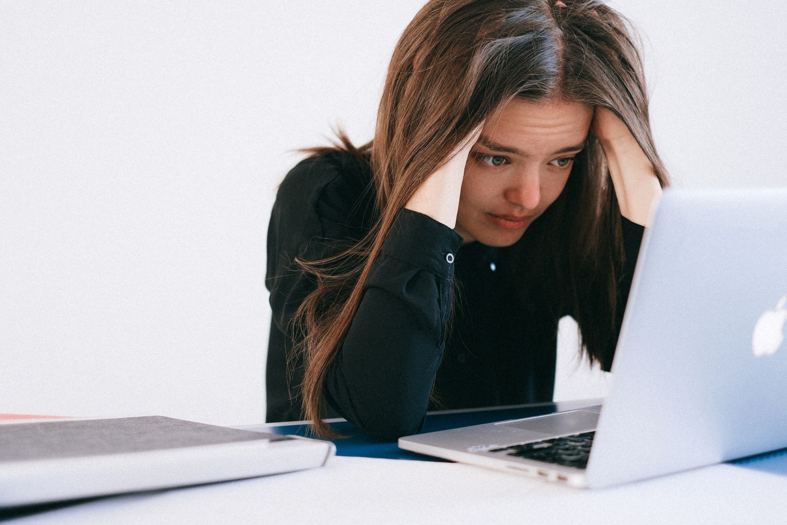 Mujer pensativa con la mano en la frente frente al computador, sosteniendo la carga mental de acordarse de todo
