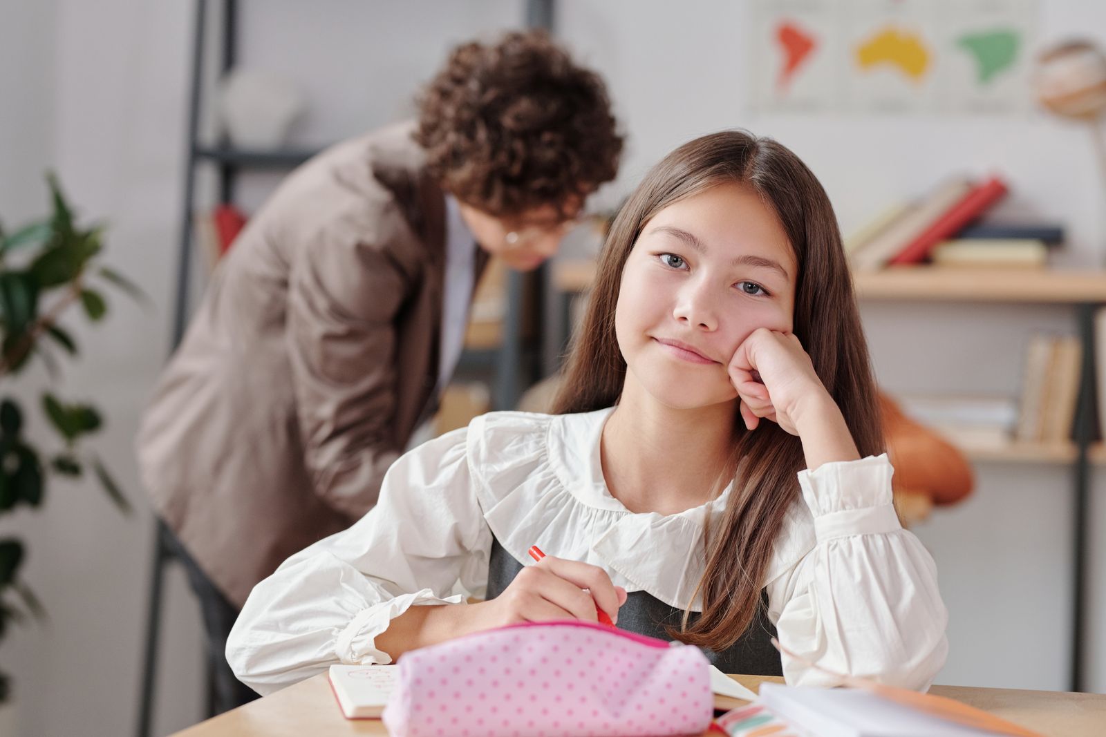 Niña distraída y soñadora en su pupitre mientras la profesora explica, una señal de TDAH en niñas