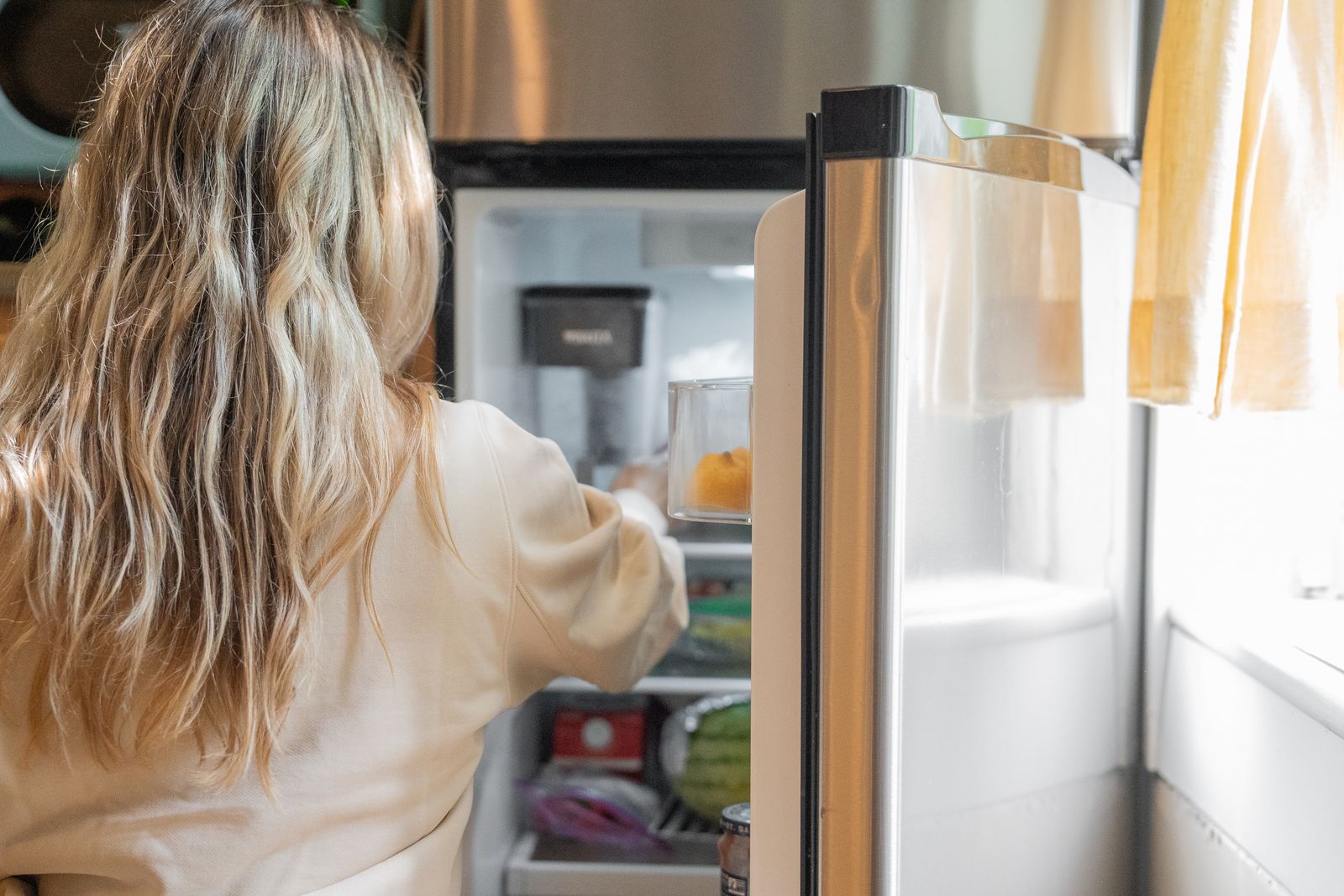 Woman looking into an open fridge, the classic ADHD object permanence moment of rediscovering forgotten food