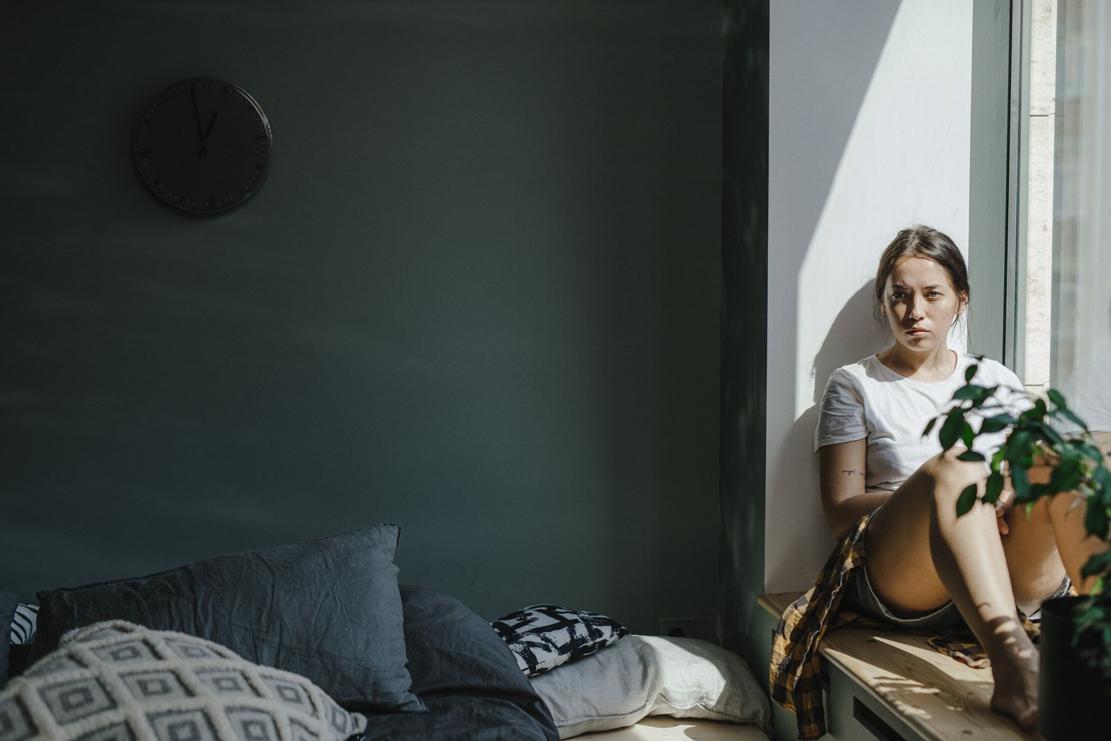 Woman sitting by the window under a wall clock, stuck in ADHD waiting mode before an appointment