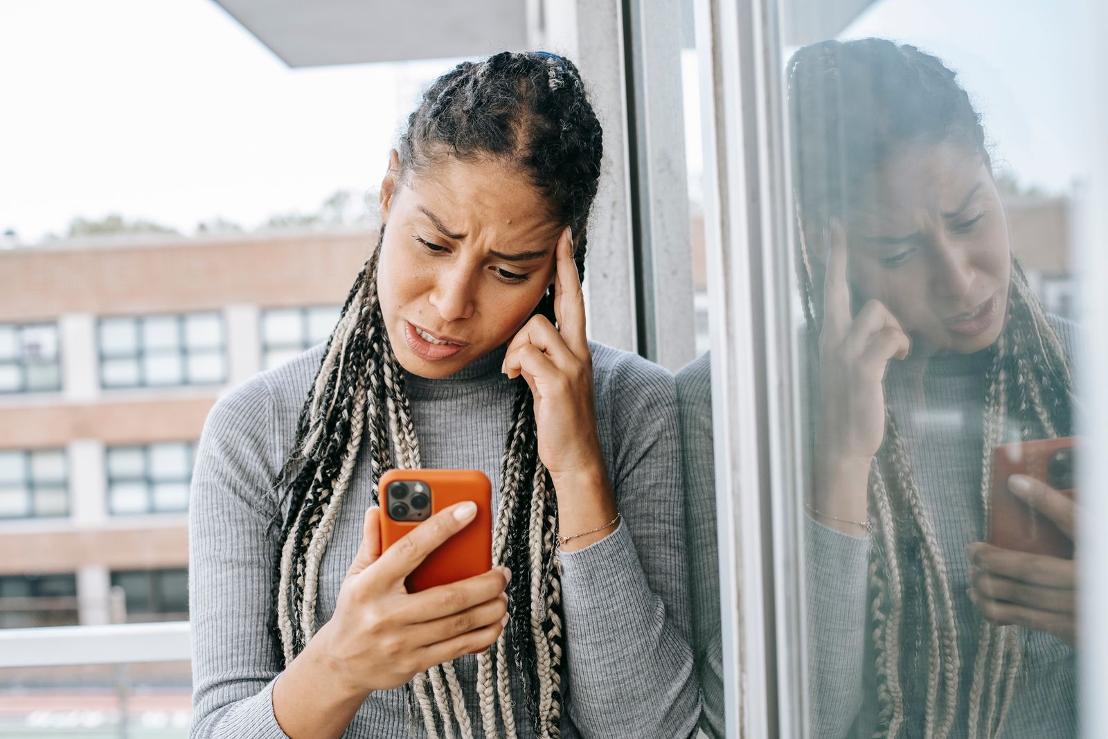 Woman sitting alone by a window, lost in thought, holding her phone